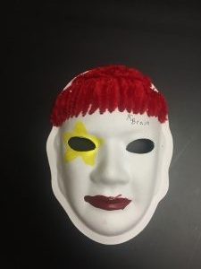 Unmasking Brain Injury mask painted with facial features and a yellow star over one eye