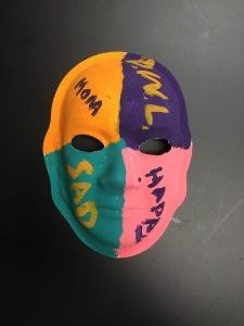Unmasking Brain Injury mask painted pink, purple, teal and orange with text in each section