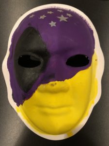 Unmasking Brain Injury mask painted part purple and black and part yellow with silver stars