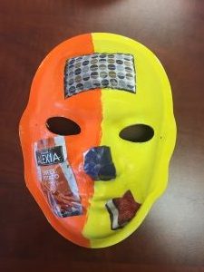 Unmasking Brain Injury mask painted half yellow and half orange with images from magazines pasted on