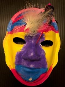 Unmasking Brain Injury mask painted with yellow, purple, blue, red and with a feather on the forehead