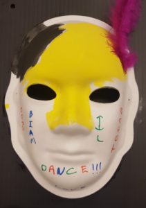 Unmasking Brain Injury mask painted with yellow and black with a red feather