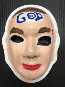 Unmasking Brain Injury mask painted with facial features with "God" painted on the forehead