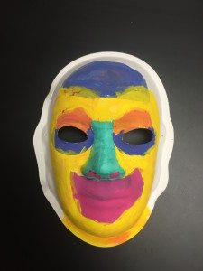 Unmasking Brain Injury mask painted with yellow, blue, teal, mauve and orange