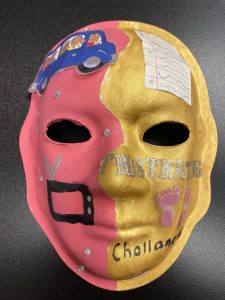 Unmasking Brain Injury mask painted gold and red with text and images on top