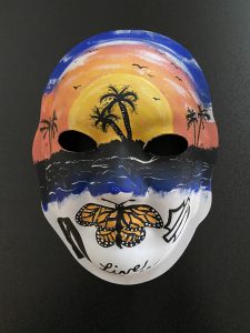 Unmasking Brain Injury mask painted with a beach sunset scene and a butterfly over the mouth