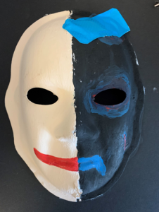 Unmasking Brain Injury mask painted half black half white with blue tape on the black side