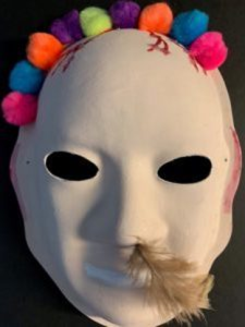 Unmasking Brain Injury mask with pompons on the top and a feather coming out of the nose