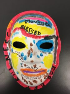 Unmasking Brain Injury mask painted with yellow, blue, red and several words