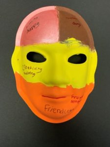 Unmasking Brain Injury mask painted with pink, brown, yellow and orange sections with text on top