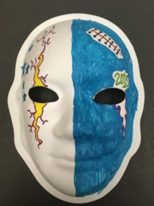 Unmasking Brain Injury mask painted half blue and with a yellow painted crack over one eye