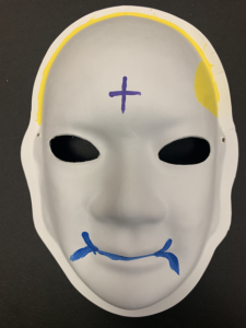 Unmasking Brain Injury mask painted with blue lips, yellow hair and a blue cross on her forehead