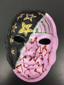 Unmasking Brain Injury mask painted black and pink with red and green lines and gold stars