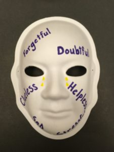 Unmasking Brain Injury mask painted with words forgetful, doubtful, clueless and helpless