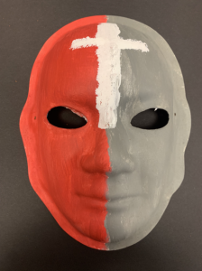 Unmasking Brain Injury mask painted gray and red with a white cross on the forehead