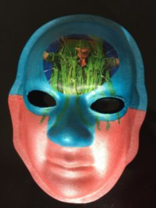Unmasking Brain Injury mask painted blue and red with a magazine cutout on the forehead
