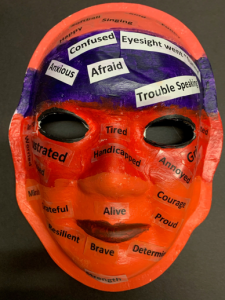 Unmasking Brain Injury mask painted red and purple with text on top