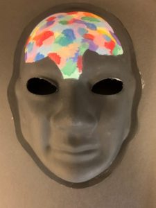 Unmasking Brain Injury mask painted gray with multicolored splotches on the forehead
