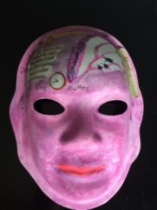 Unmasking Brain Injury mask painted purple with collage on the forehead