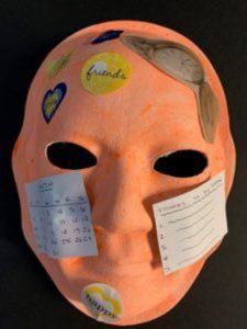 Unmasking Brain Injury mask painted orange with papers collaged on top