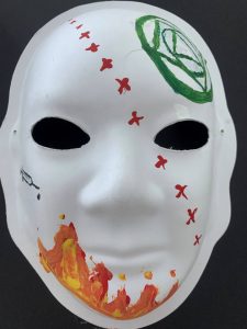 Unmasking Brain Injury mask painted with fire, a syringe, red xs and a green design on the forehead