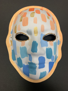 Unmasking Brain Injury mask painted white with orange and blue splotches
