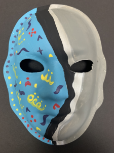 Unmasking Brain Injury mask painted with blue, gray, black and white with yellow, black and red pattern on the blue