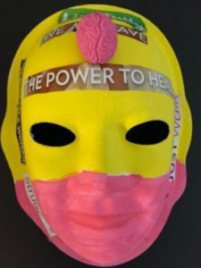 Unmasking Brain Injury mask painted pink and yellow with text cut from magazines