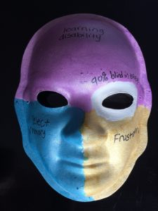 Unmasking Brain Injury mask painted with purple, gold and blue sections with text