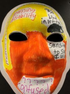 Unmasking Brain Injury mask painted with orange and yellow with text on top