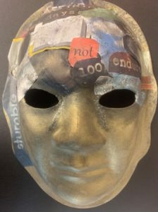 Unmasking Brain Injury mask painted in gold with magazine text collaged on it