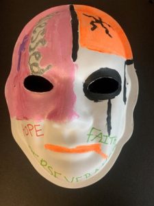 Unmasking Brain Injury mask painted with pink, orange and white sections with text