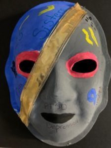 Unmasking Brain Injury mask painted in blue and gray with a gold ribbon diagonally separating them