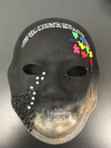 Unmasking Brain Injury mask painted black and gold with puzzle pieces and rhinestones