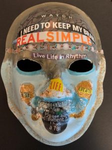 Unmasking Brain Injury mask painted with pale blue and brown with brain injury stickers
